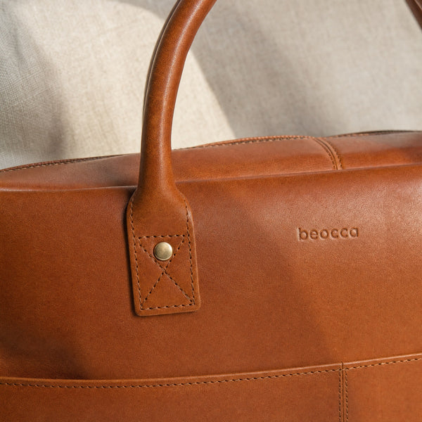 Detail van het gerolde hengsel en de klinknagel van de Beocca Mason laptoptas in cognac